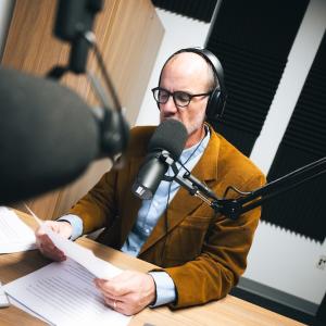Michael Kramp sits in a podcast studio speaking into a microphone.  