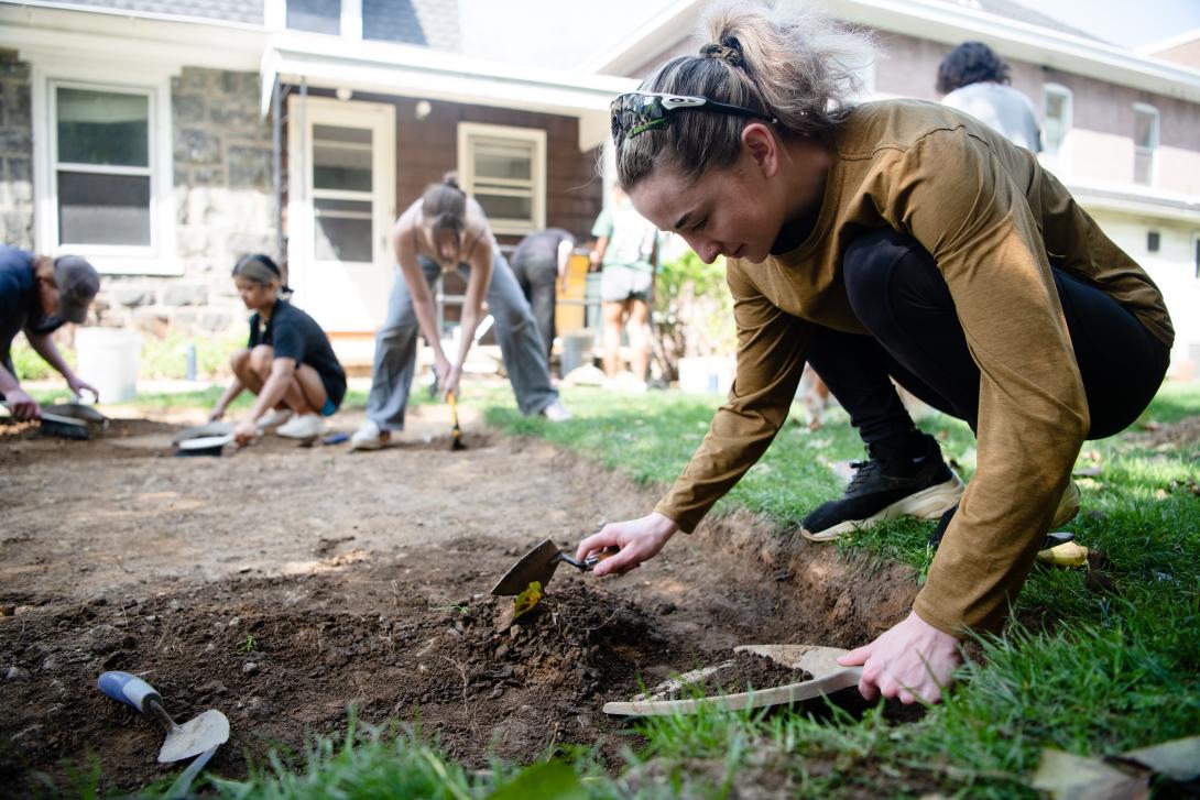 A student excavates the ground outside the Humanities Center