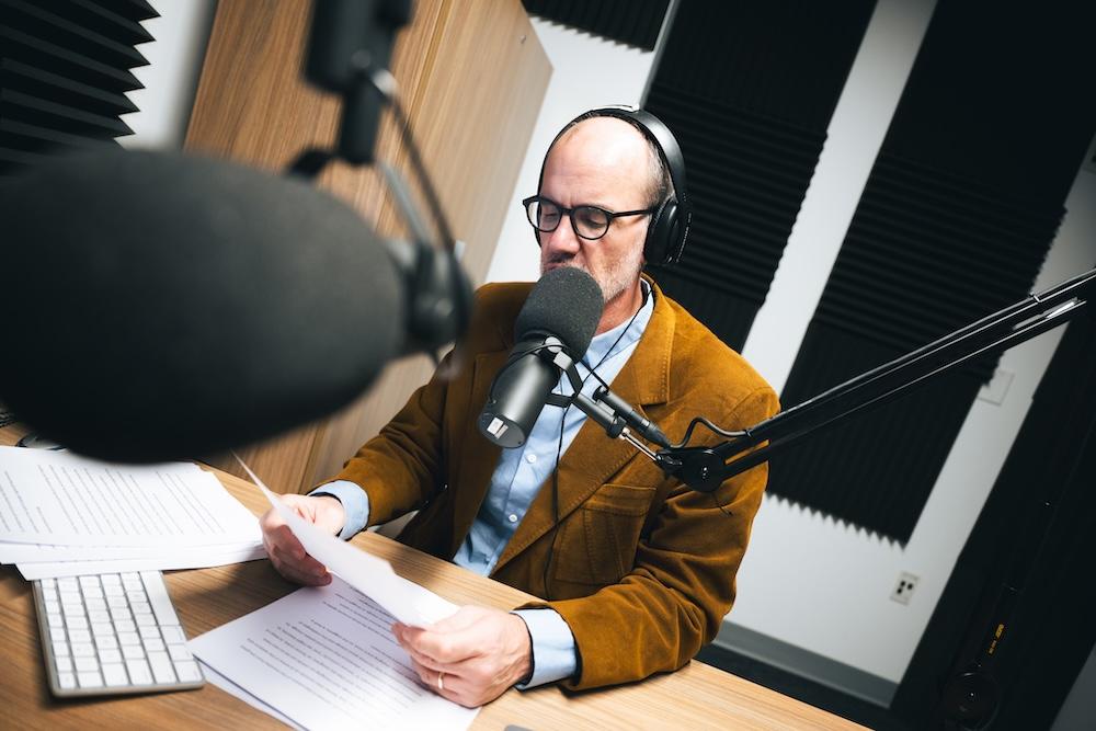 Michael Kramp sits in a podcast studio speaking into a microphone.  